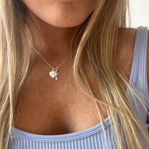 Op de afbeelding: Een zilveren ketting met een hartvormige hanger en een sleutel hanger. De hartvormige hanger heeft een kleine inscriptie.