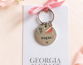 May include: A silver-toned metal keychain featuring a round disc stamped with the name Megan and a small heart, a smaller disc with the number 21 and a heart, and a cocktail glass charm. The keychain is attached to a white card labeled GEORGIA & GRACE.