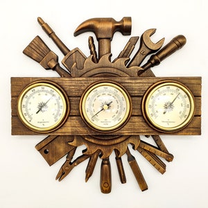 May include: A wooden wall clock with three round analog gauges. The gauges are surrounded by a decorative design of various tools, including a hammer, wrench, saw, and screwdriver. The gauges measure humidity, temperature, and barometric pressure.