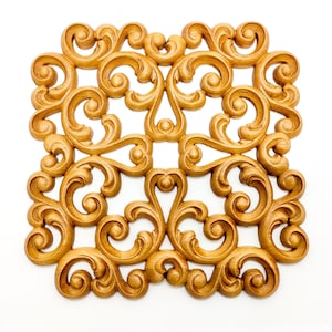 May include: A gold-coloured metal wall decor with a square shape and intricate scrollwork design.