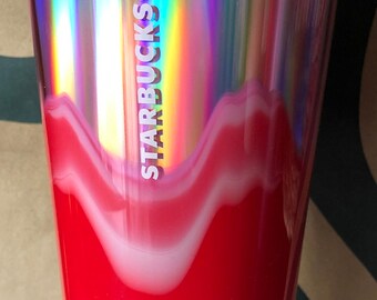 May include: A pink and white iridescent Starbucks tumbler with a red and white swirl design. The tumbler has a pink lid and a pink straw.