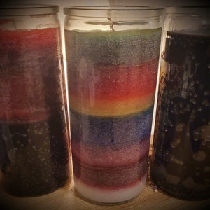 May include: Three glass candle jars with colorful layered wax. The candle on the left has red, black, and white layers. The middle candle has rainbow colored layers. The candle on the right has black and white layers.