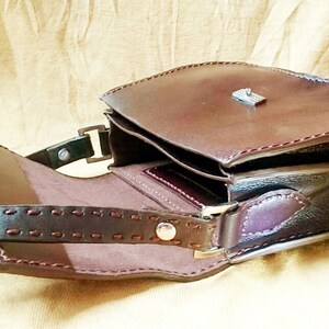 May include: A brown leather satchel bag with a flap closure and a metal clasp. The bag has a shoulder strap and is open to reveal the interior.