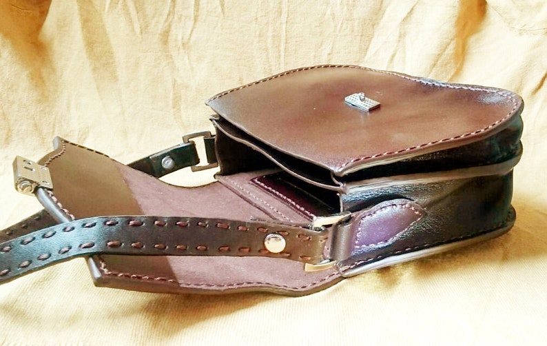 May include: A brown leather satchel bag with a flap closure and a metal clasp. The bag has a shoulder strap and is open to reveal the interior.
