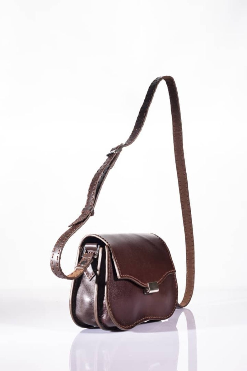 May include: A brown leather crossbody bag with a flap closure and a silver buckle. The bag has a long adjustable strap.