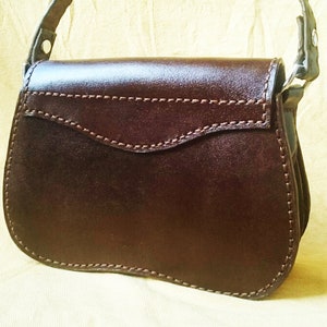 May include: A brown leather handbag with a flap closure and a single strap. The bag has a stitched design and a smooth finish.