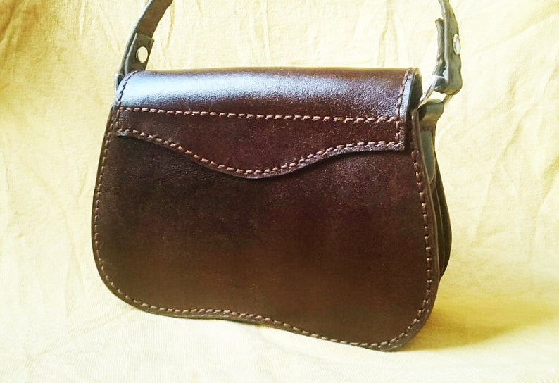 May include: A brown leather handbag with a flap closure and a single strap. The bag has a stitched design and a smooth finish.