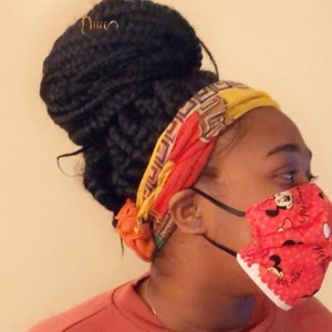 May include: A person wearing a red and yellow patterned headband and a red face mask with a white border and a Minnie Mouse design. The mask has white polka dots and the text "Make a Wish" on the bottom.