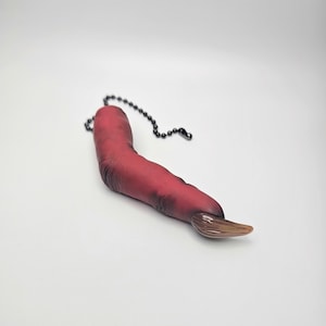 May include: A novelty light pull in the shape of a severed finger. The finger is a deep red color with a brown fingernail. A black chain is attached to the finger.
