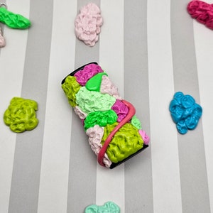 May include: A colorful, multi-colored, abstract, polymer clay bead with a pink, green, and white design. The bead is wrapped with a pink ribbon and has a black base.
