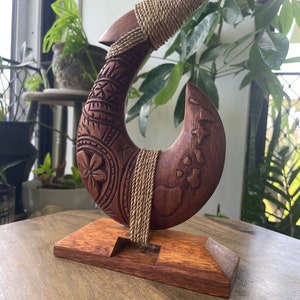 Ein detailliertes, handgeschnitztes Makau aus massivem Hibiskusholz mit floralen Tribalmotiven und Karte der hawaiianischen Inseln auf einem Sockel.