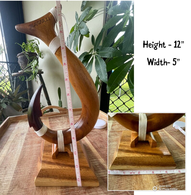 May include: A wooden Hawaiian-style fish hook sculpture. The sculpture is 12 inches tall and 5 inches wide. It features a curved design with a dark brown hook and a lighter brown body, with the word "HAWAII" carved into the top.