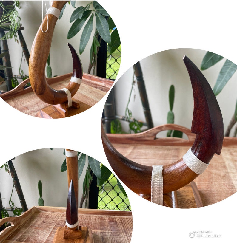 May include: A handcrafted wooden sculpture with a curved, horn-like shape. The sculpture features a dark brown tip and a lighter brown body, accented with a white fabric band. It is mounted on a small wooden base.