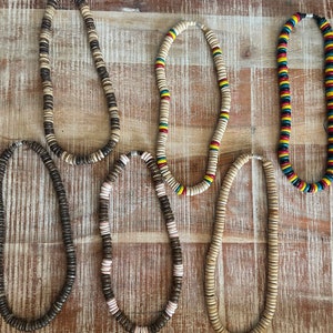 May include: Several handcrafted necklaces with wooden beads in various colours and designs. Some necklaces feature natural wood tones, while others incorporate colourful accents like red, yellow, and blue. The beads are strung together, creating a casual, bohemian style.