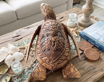 May include: A hand-carved wooden sea turtle sculpture featuring intricate shell detailing with two smaller turtles embossed on the center. The natural brown wood grain is visible throughout the textured surface of the turtle's head, flippers, and shell.