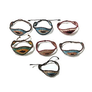May include: A collection of handmade macrame bracelets in various colors, including brown, blue, and red. Each bracelet features a woven design with intricate patterns. The bracelets are displayed on a white surface, showcasing their unique craftsmanship.