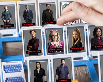 May include: A game board with character cards featuring photos of the cast of the TV show Criminal Minds. The cards are arranged in a grid with the names "Derek", "Aaron", "David", "Spencer", "Penelope", "Jennifer", "Tara", and "Luke" printed below each photo.