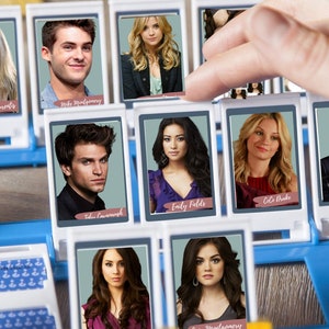 Könnte beinhalten: Ein blaues und weißes Spielbrett mit verschiedenen Charakterkarten mit Fotos der Besetzung der Fernsehserie Pretty Little Liars. Die Karten enthalten die Namen der Charaktere: Alison DiLaurentis, Mike Montgomery, Emily Fields, Cole Drake, Jason DiLaurentis, Toby Cavanaugh, Aria Montgomery und Spencer Hastings.