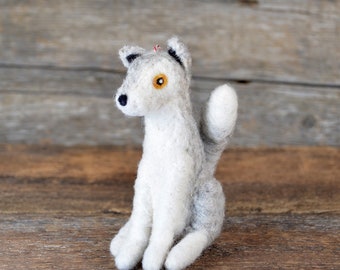 May include: A gray and white felt wolf figurine with black eyes and a yellow nose. The wolf is sitting with its tail curled up behind it.