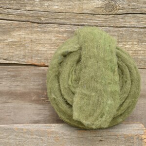 May include: A tightly wound roll of green wool yarn on a wooden surface.