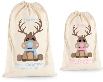 May include: Two personalized Christmas gift bags with a reindeer design. The bag on the left has a blue scarf and the text "Harry's First Christmas - 2019 -" The bag on the right has a pink scarf and the text "Emily's First Christmas - 2019 -"