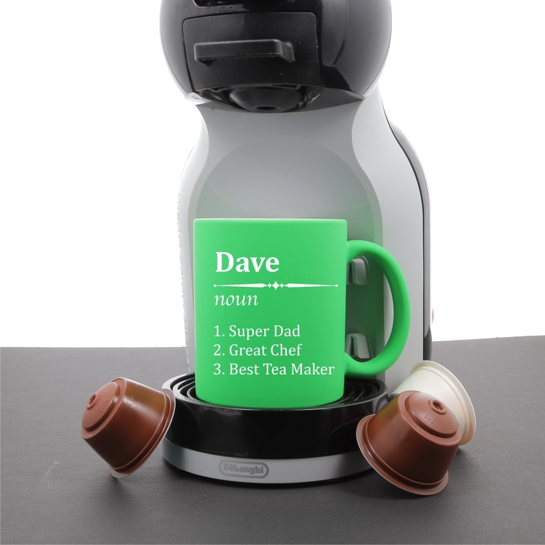 May include: Green ceramic mug with a white inscription that reads "Dave noun 1. Super Dad 2. Great Chef 3. Best Tea Maker". The mug is sitting on a black and silver coffee maker.