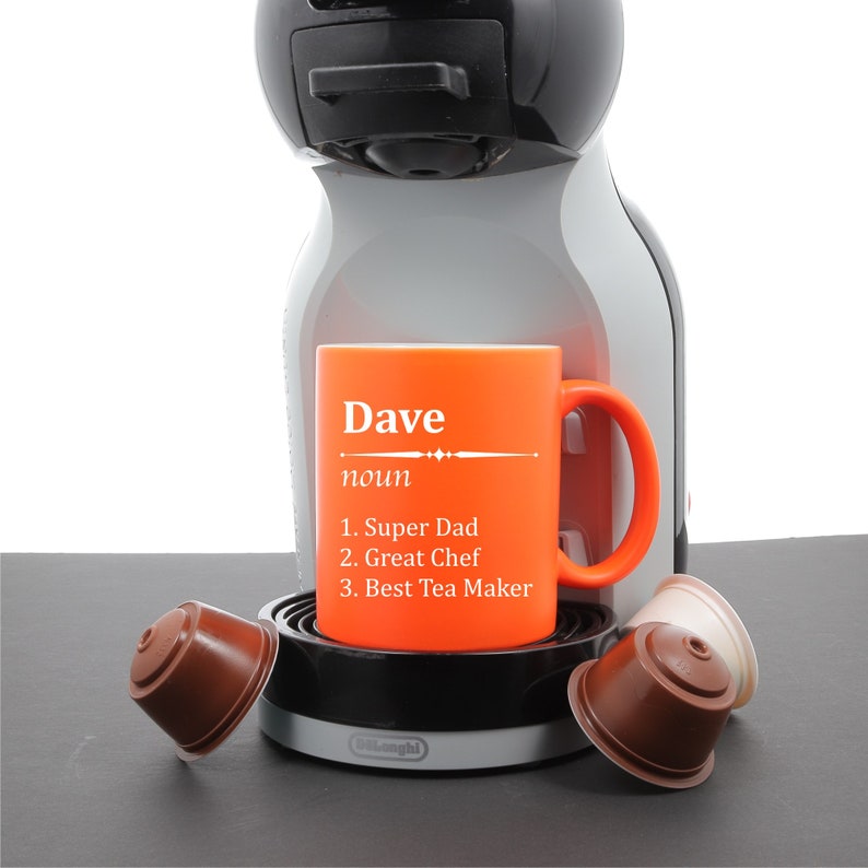 May include: Orange mug with the name "Dave" and the definition "noun 1. Super Dad 2. Great Chef 3. Best Tea Maker" on it. The mug is sitting on a coffee machine with coffee pods.
