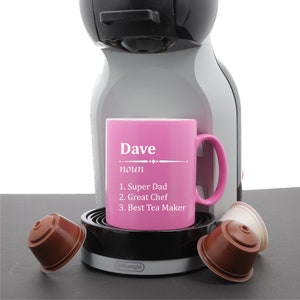 May include: Pink coffee mug with the word "Dave" and the definition "noun 1. Super Dad 2. Great Chef 3. Best Tea Maker" on it. The mug is sitting on a coffee machine.