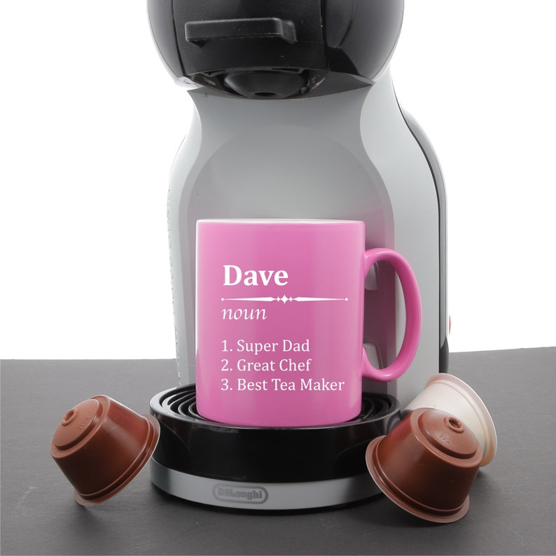 May include: Pink coffee mug with the word "Dave" and the definition "noun 1. Super Dad 2. Great Chef 3. Best Tea Maker" on it. The mug is sitting on a coffee machine.
