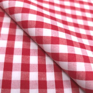 May include: Close-up of red and white checkered fabric. The fabric is folded, showing the pattern's repeating squares. The red squares alternate with white squares, creating a classic gingham design. The fabric appears to be cotton or a similar material.