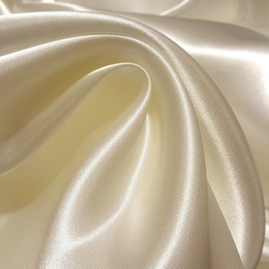 May include: Close-up of a smooth, ivory-colored satin fabric with a soft, flowing drape.