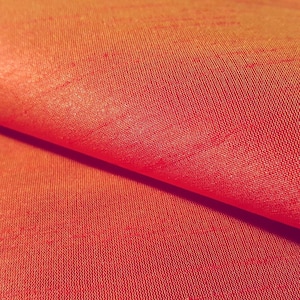 May include: Close-up of a vibrant orange-red fabric with a subtle sheen. The material is tightly woven, with visible texture and a slight fold creating shadows. The color gradient shifts from a brighter orange to a deeper red.