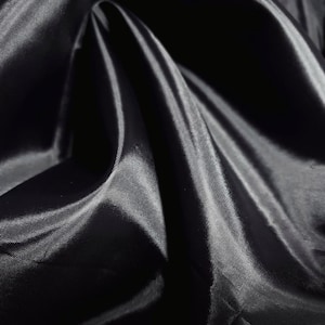 May include: Close-up of a black fabric with a satin sheen. The fabric is draped, creating folds and shadows that highlight its texture and luster. The material appears smooth and flowing, reflecting light.