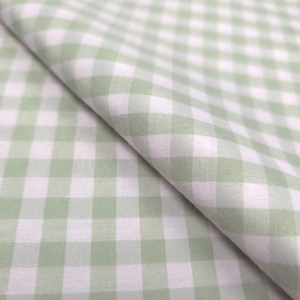 May include: Close-up of a fabric with a gingham pattern in light green and white. The fabric is folded, showing the texture and the repeating square design. The fabric is likely cotton or a similar material.