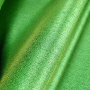 May include: Close-up of a vibrant green fabric with a subtle sheen. The material has a textured surface with visible threads and folds, creating depth and dimension. The bright, solid color suggests a textile suitable for apparel or home decor.