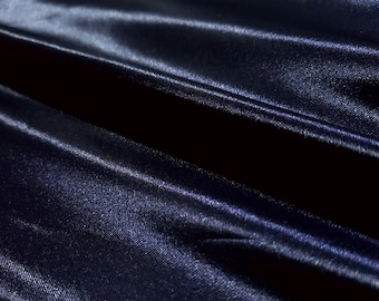 May include: Close-up of a dark blue satin fabric with a smooth, silky texture. The fabric is folded and draped, creating soft, flowing lines.