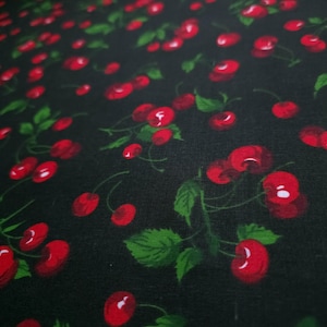 May include: Close-up of a fabric with a repeating pattern of red cherries and green leaves on a black background. The cherries have white highlights, and the leaves have detailed veining.