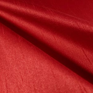 May include: Close-up of a vibrant red fabric with a silky sheen. The material is folded, creating shadows and highlights that emphasize its texture. The fabric appears smooth and luxurious, suitable for apparel or home decor.
