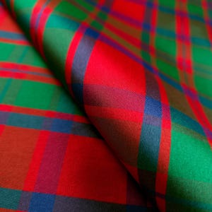 May include: A folded piece of fabric featuring a classic tartan plaid pattern. The textile displays a vibrant color palette of bright red, emerald green, and deep navy blue stripes that intersect to form a repeating geometric grid design.