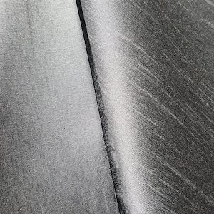 May include: Close-up of two pieces of black fabric with a subtle textured pattern. The fabric on the left has a finer weave than the fabric on the right.