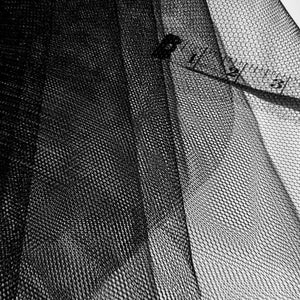 May include: Black mesh fabric with a fine, hexagonal pattern. The fabric is folded and a ruler is visible in the background.