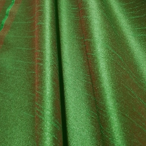 May include: A close-up of a green fabric with a subtle sheen. The fabric is folded and has a smooth, silky texture.
