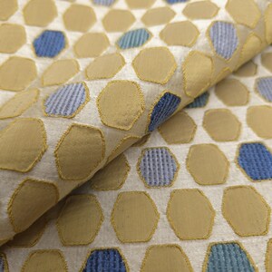 K&ouml;nnte beinhalten: Nahaufnahme eines Stoffes mit einem sich wiederholenden Muster aus beige und blauen sechseckigen Formen. Die Formen sind mit einem goldenen Faden umrandet, vor einem hellbeigen Hintergrund. Der Stoff hat ein strukturiertes Aussehen.
