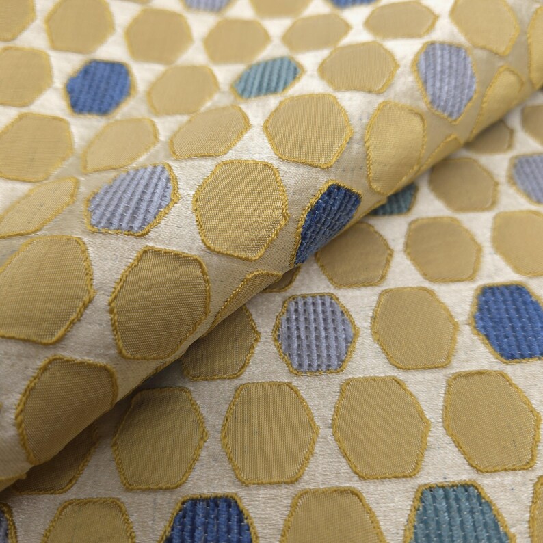 K&ouml;nnte beinhalten: Nahaufnahme eines Stoffes mit einem sich wiederholenden Muster aus beige und blauen sechseckigen Formen. Die Formen sind mit einem goldenen Faden umrandet, vor einem hellbeigen Hintergrund. Der Stoff hat ein strukturiertes Aussehen.