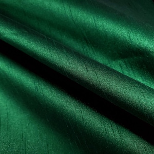 May include: A close-up of a deep green fabric with a subtle sheen. The fabric has a smooth, silky texture and a slightly wrinkled appearance.