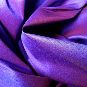 K&ouml;nnte beinhalten: Nahaufnahme eines tiefvioletten Stoffes mit einem dezenten Glanz. Der Stoff ist gefaltet und drapiert und erzeugt weiche, flie&szlig;ende Linien.