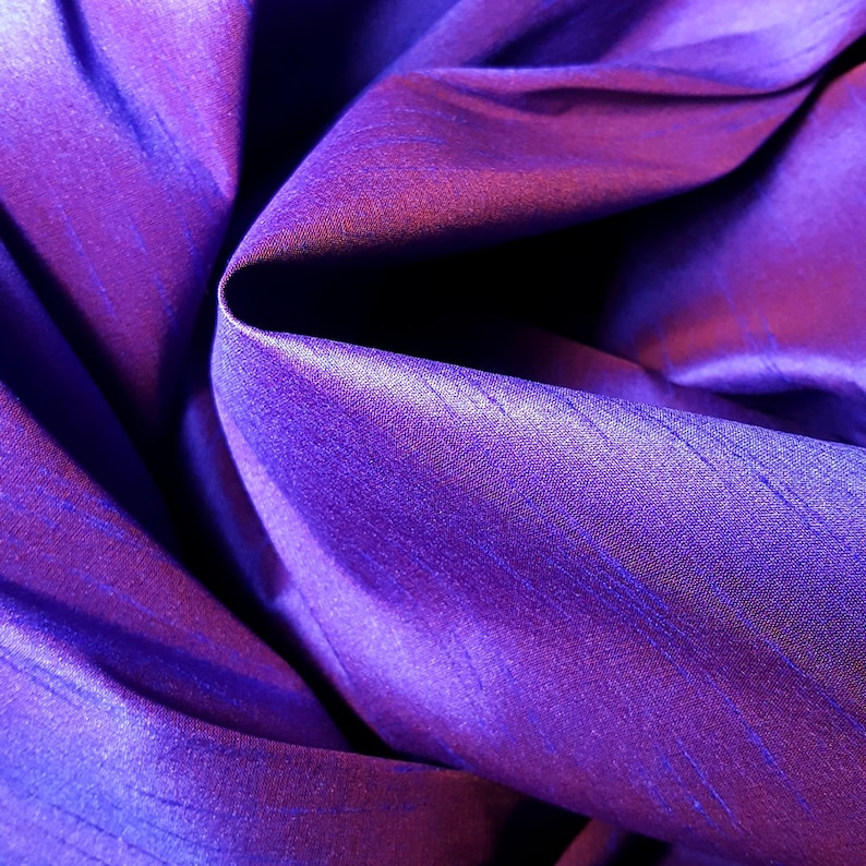 K&ouml;nnte beinhalten: Nahaufnahme eines tiefvioletten Stoffes mit einem dezenten Glanz. Der Stoff ist gefaltet und drapiert und erzeugt weiche, flie&szlig;ende Linien.