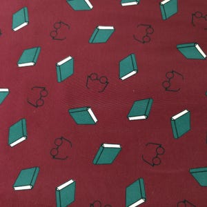 May include: Burgundy fabric with a repeating pattern of teal books and black eyeglasses. The books have white pages and are scattered across the background. The eyeglasses are simple line drawings.