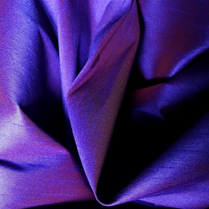 K&ouml;nnte beinhalten: Nahaufnahme eines tiefvioletten Stoffes mit einem subtilen, schimmernden Glanz. Der Stoff ist drapiert und gefaltet und erzeugt weiche, flie&szlig;ende Linien.