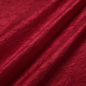 May include: Close-up of a deep red fabric with a crinkled texture. The material has a slight sheen, with folds and shadows creating depth. The fabric appears to be lightweight and flowing, suitable for apparel or decorative purposes.